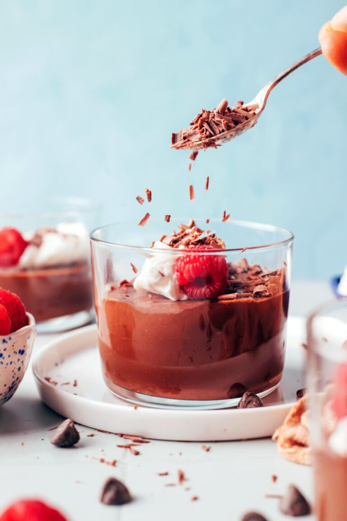 Polvilhar chocolate amargo ralado em um copo de creme de leite coberto com chantilly de coco e framboesa fresca